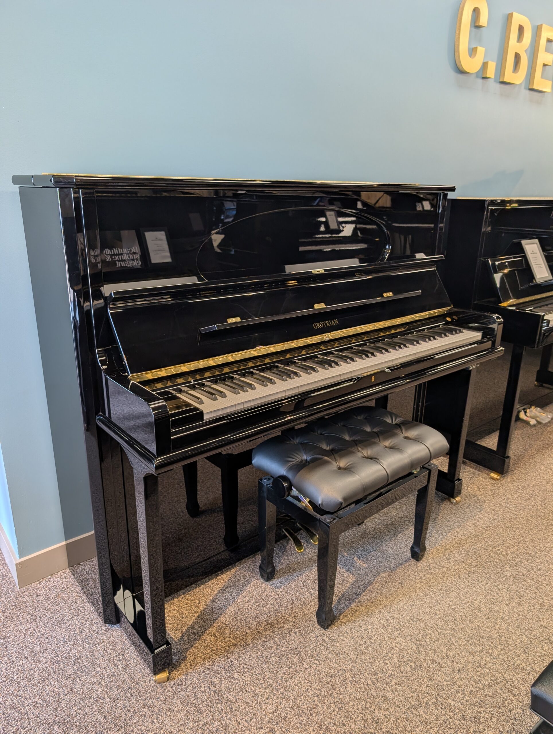 Glossy black Grotrian Pianos are displayed with a tufted bench in Calgary